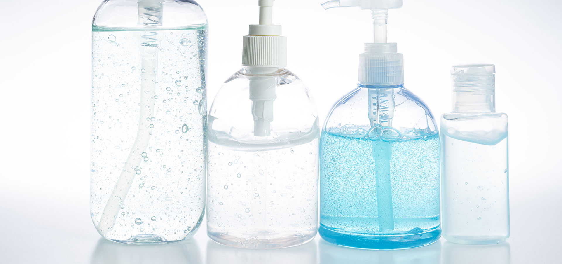 Four bottles of hand sanitizer in different sizes, the largest three with pump dispensers, the travel sized bottle has a flip top dispenser